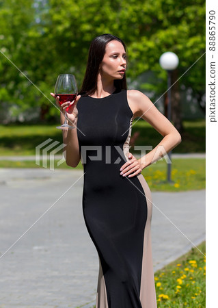 Elegant woman with glass of wine walking in garden of mansion 88865790