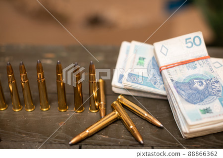 Paper banknotes and rifle cartridges lie on a crate. 88866362