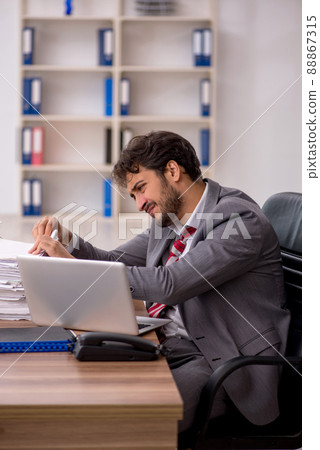 Young male employee unhappy with excessive work in the office Young male employee unhappy with excessive work in the office 88867315