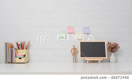Chalkboard, potted plant and stationery on white table against brick wall. Copy space for your information content. 88872498