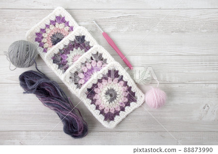 Granny squares crochet in pink and purple shades, a hook and yarn balls 88873990