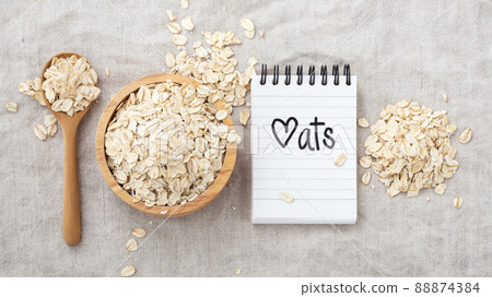 Oat flake cereal in wooden bowl with oats word on notebook on linen cloth background, top view 88874384