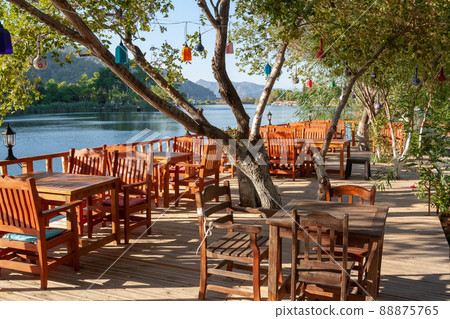 Wooden empty tables in a restaurant on the river bank. Tree with colored lanterns. Wooden empty tables in a restaurant on the river bank. Tree with colored lanterns. 88875765