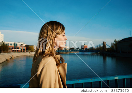 Millennial caucasian woman standing at riverfront and enjoy with sunny day, Female tourist wearing stylish trench walking at european city street Millennial caucasian woman standing at riverfront and enjoy with sunny day, Female tourist wearing stylish trench walking at european city street 88875970
