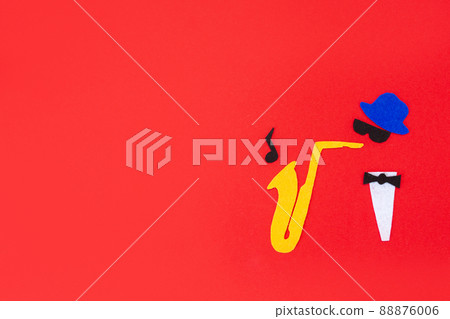 Jazz Day. Silhouette of a musician with a saxophone from which melodies flew out, on a red background, cutted out of felt. Flat lay. Copy space Jazz Day. Silhouette of a musician with a saxophone from which melodies flew out, on a red background, cutted out of felt. Flat lay. Copy space 88876006