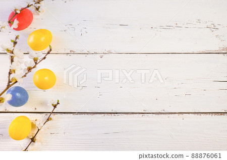 Colorful Easter eggs with spring bloom flowers and green leaves, on a white wooden background. Space for text 88876061