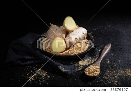 Pieces of ginger and ginger powder in wooden spoon and plate on black background. Pieces of ginger and ginger powder in wooden spoon and plate on black background. 88876197