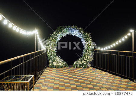 Round wedding arch decorated with fresh flowers. Evening ceremony 88877473