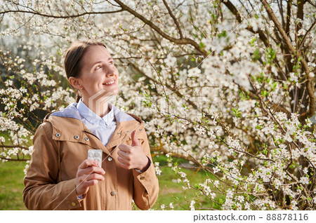 Woman allergic suffering from seasonal allergy at spring, posing in blossoming garden at springtime. Young happy woman using allergy drug, showing thumbs up. Antihistamine medication concept 88878116