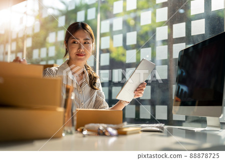 Young Asian small business owner working at home office, taking note on purchase orders. Online marketing packaging delivery, startup SME entrepreneur or freelance woman concept Young Asian small business owner working at home office, taking note on purchase orders. Online marketing packaging delivery, startup SME entrepreneur or freelance woman concept 88878725