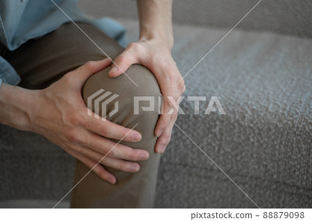 Man massages knee feeling acute joint pain sitting on sofa Man massages knee feeling acute joint pain sitting on sofa 88879098