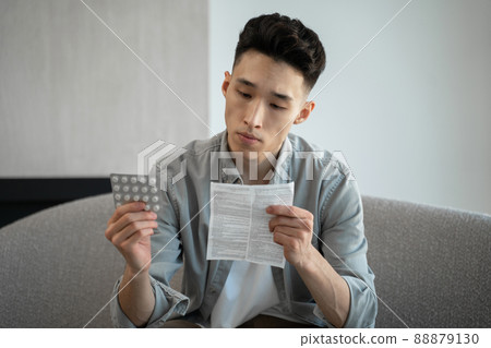 Asian man reads instructions for use of pills for headache 88879130
