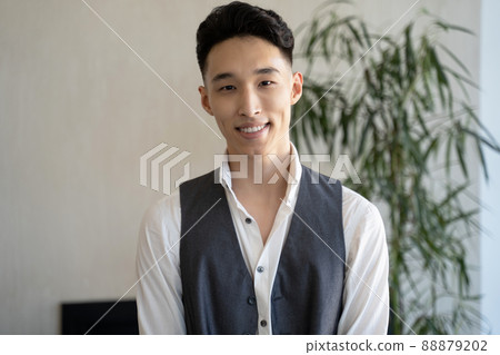 Young Asian man looks in camera smiling against lush plant Young Asian man looks in camera smiling against lush plant 88879202