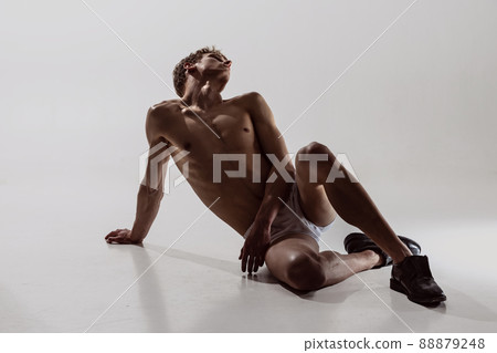 Portrait of young handsome shirtless sportive man sitting on floor isolated on grey background. Wellness, art, beauty of male beauty concept. Portrait of young handsome shirtless sportive man sitting on floor isolated on grey background. Wellness, art, beauty of male beauty concept. 88879248