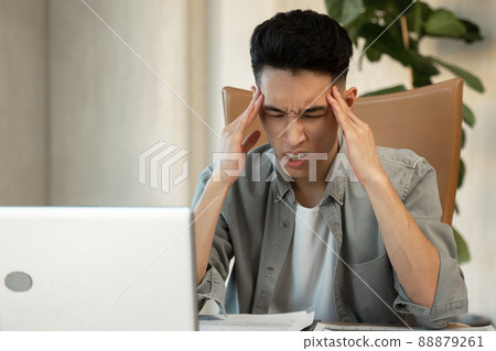 Asian employee holds head trying to solve difficult issue Asian employee holds head trying to solve difficult issue 88879261