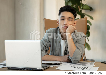 Tired Asian man sits in office propping up head with hand Tired Asian man sits in office propping up head with hand 88879266