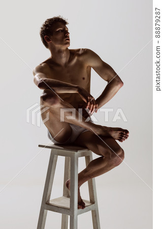 Looks sad, serious. One young shirtless sportive man in white boxer-briefs sitting on high chair isolated on grey background. Art, fashion, diversity, emotions Looks sad, serious. One young shirtless sportive man in white boxer-briefs sitting on high chair isolated on grey background. Art, fashion, diversity, emotions 88879287