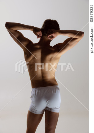Back view of young shirtless muscled man wearing white boxer-briefs standing isolated on gray background. Natural beauty of male body 88879322