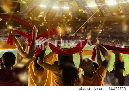Victory. Back view of football, soccer fans cheering their team with scarfs at crowded stadium at evening time. Concept of sport, competition. Out of focus effect Victory. Back view of football, soccer fans cheering their team with scarfs at crowded stadium at evening time. Concept of sport, competition. Out of focus effect 88879753
