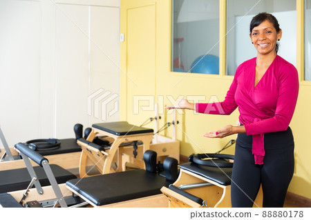 Friendly Hispanic female fitness instructor inviting to pilates reformer studio 88880178