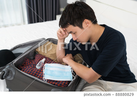 stress man packing suitcase luggage including face mask and alcohol spray to protect coronavirus (covid-19) on bed 88880829