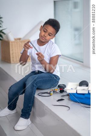 A dark-skinned boy playing with a toy near the window 88881210