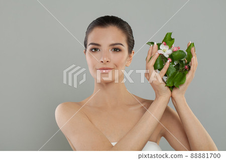 Beautiful young woman with clean fresh skin showing spring flowers. Facial treatment 88881700