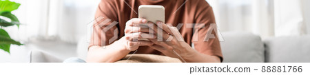 Technology Concept The man sitting next to a pot of plant, putting a small pillow on his lap, and checking something on his smartphone Technology Concept The man sitting next to a pot of plant, putting a small pillow on his lap, and checking something on his smartphone 88881766