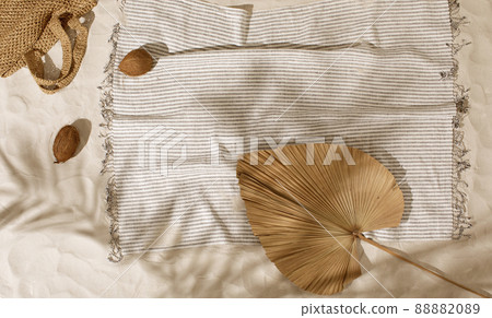 Striped linen beach towel with fringes and two coconuts on sandy beach with shadows from palm tree. Relaxation and tropical summer holidays concept Striped linen beach towel with fringes and two coconuts on sandy beach with shadows from palm tree. Relaxation and tropical summer holidays concept 88882089