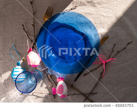 Easter table setting empty blue glass plate cutlery tree branches linen cloth flat lay harsh shadow Festive dish place 88883701