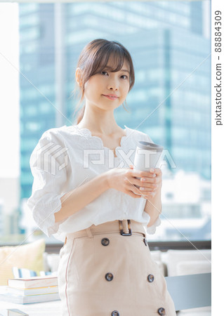 A young woman standing in the office with a tumbler in her hand A young woman standing in the office with a tumbler in her hand 88884309
