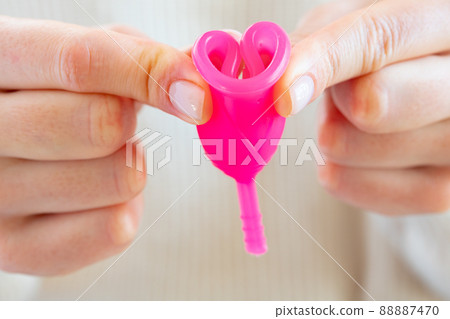 Woman in white sweater holding pink menstrual cup in hands close up 88887470