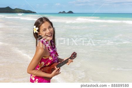 Hawaii luau ukulele hula dancing woman playing guitar on beach vacation with flower lei necklace and paero. Asian dancer smiling on hawaiian travel vacation 88889580