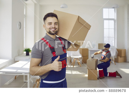 Smiling male worker of moving and delivery company holding cardboard box showing thumbs up. Smiling male worker of moving and delivery company holding cardboard box showing thumbs up. 88889678
