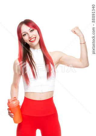 A beautiful, athletic, slim, smiling and cheerful woman in a white top and red sweatpants demonstrates her biceps and holds a bottle of water. Lifestyle concept with sports and gym, healthy lifestyle A beautiful, athletic, slim, smiling and cheerful woman in a white top and red sweatpants demonstrates her biceps and holds a bottle of water. Lifestyle concept with sports and gym, healthy lifestyle 88891340