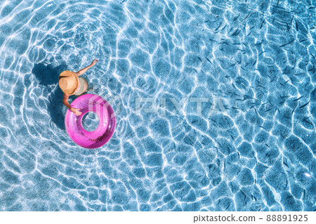 Aerial view of a young woman in hat swimming with pink swim ring in blue sea with school of fish 88891925