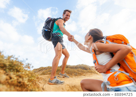 People hiking man helping woman climbing up hill on mountain hike. Helping hand team support friend supporting success trek for girl 88894725