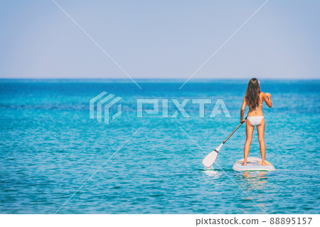 Paddle board bikini woman standing paddling away on stand up paddleboarding on ocean blue background water. Hero view of girl standing on sup surfboard watersport leisure activity Paddle board bikini woman standing paddling away on stand up paddleboarding on ocean blue background water. Hero view of girl standing on sup surfboard watersport leisure activity 88895157