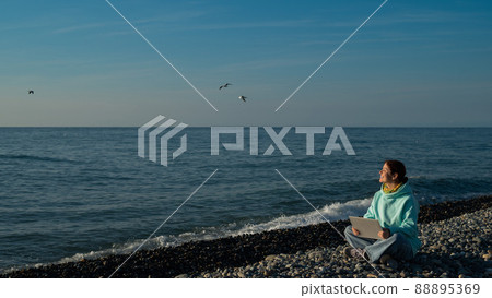 Happy caucasian woman working on a laptop while sitting on a pebble beach. 88895369