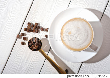 cup of cappuccino coffee on white wooden table and coffee beans, having a break, time for relax and digital detox top view. cup of cappuccino coffee on white wooden table and coffee beans, having a break, time for relax and digital detox top view. 88895847