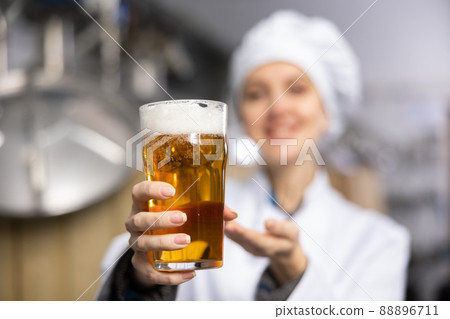 Glass of foamy amber ale in hands of female brewer 88896711