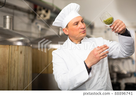 Focused brewer checking quality of hop pellets in brewery 88896741