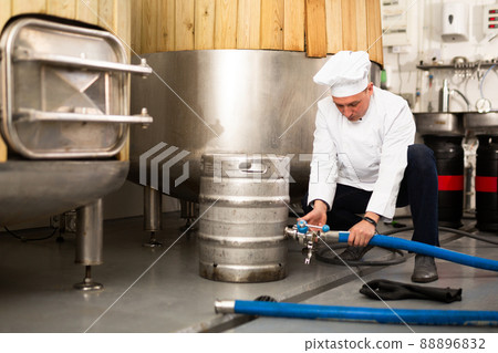 Brewer connecting hose to keg to fill with beer in brewery 88896832