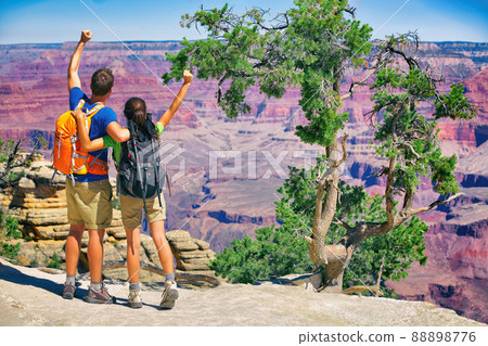 Grand Canyon hikers tourists couple cheering success with arms up happy for hike achievement. Backpackers hiking with backpacks standing at view of famous american landmark, USA trip travel. 88898776
