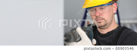 Man in construction helmet and glasses drills wall 88903546