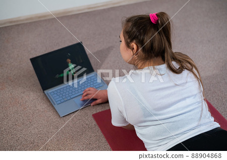 A chubby young woman is watching an online fitness lesson on a laptop. Distance sports training. A chubby young woman is watching an online fitness lesson on a laptop. Distance sports training. 88904868