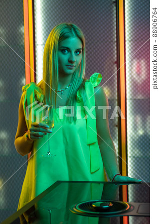 Blonde girl in smart dress standing with glass of sparkling wine in home kitchen Blonde girl in smart dress standing with glass of sparkling wine in home kitchen 88906764