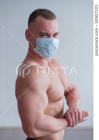 Bodybuilder with a naked torso in a medical mask. Muscled with a guy doing sports in quarantine. Respiratory protection. 88907205
