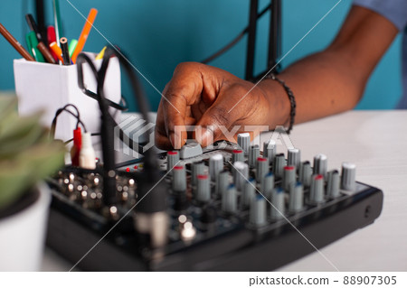 Closeup of content creator hand adjusting master volume fader on mixer console on desk during live podcast. Vlogger working on sound settings of equilizer used to broadcast live stream. Closeup of content creator hand adjusting master volume fader on mixer console on desk during live podcast. Vlogger working on sound settings of equilizer used to broadcast live stream. 88907305
