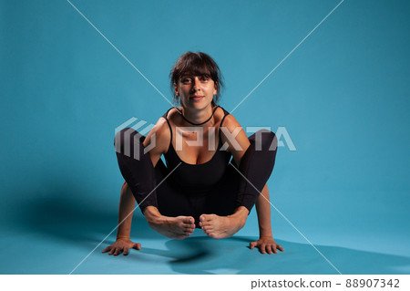 Personal trainer standing in hands with crossed legs practicing yoga position working at healthy lifestyle. Fit athletic person in sportwear stretching body muscles durinmg sport workout 88907342